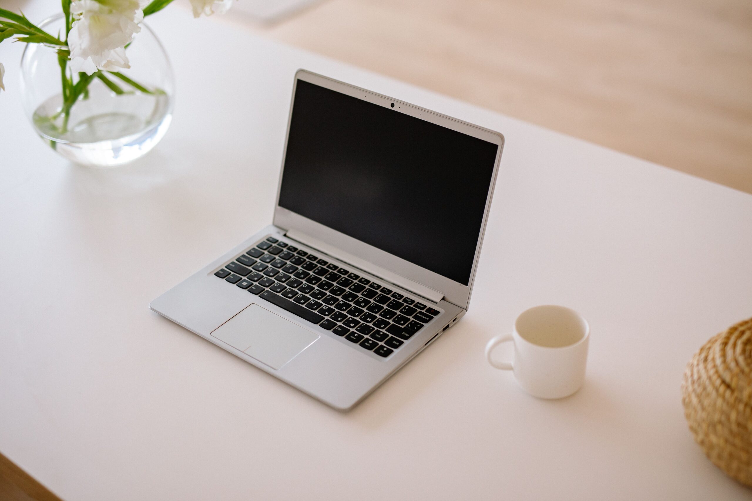 A minimalist workspace with an open laptop, coffee mug, and vase on a bright indoor table.