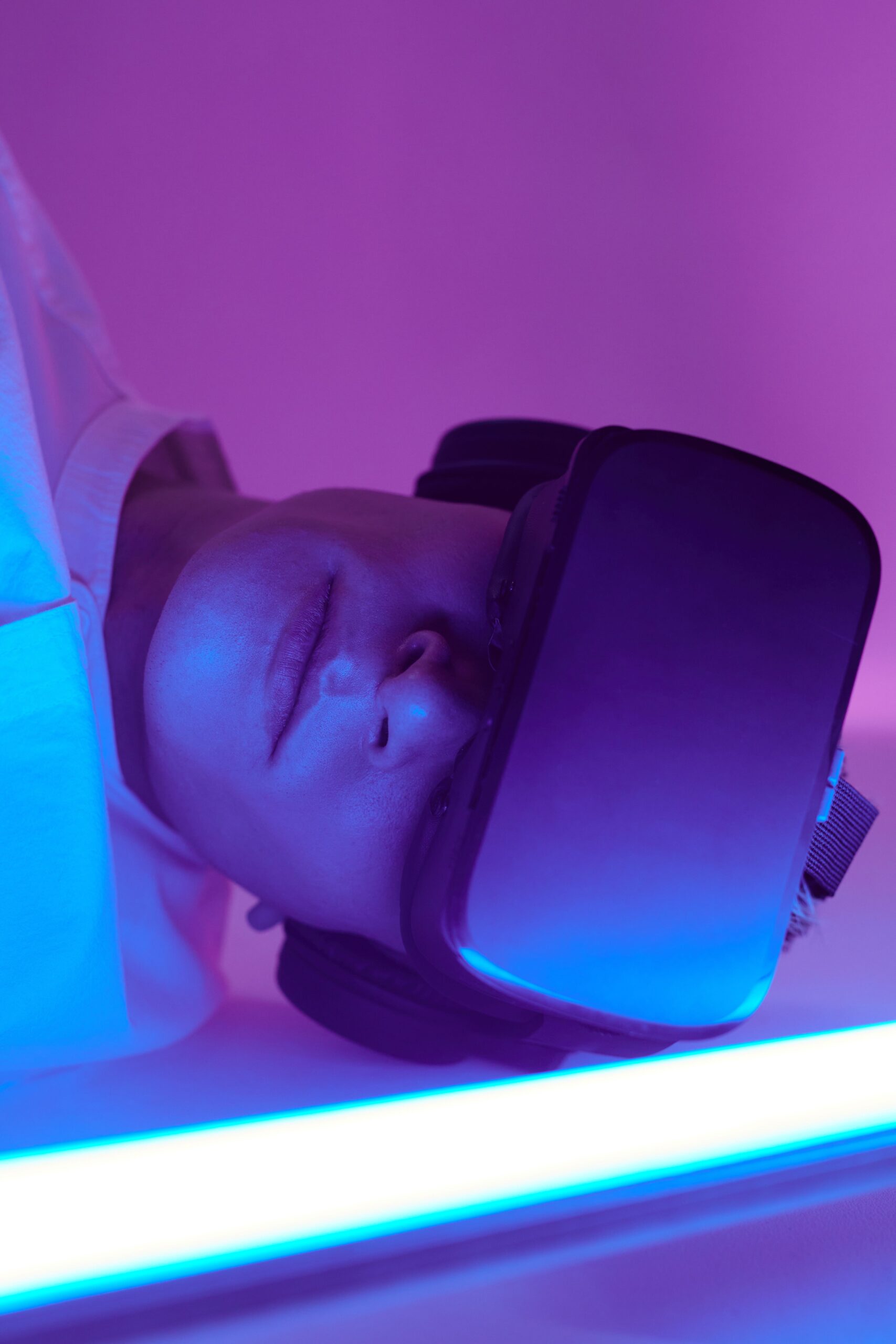 Person immersed in virtual reality wearing VR headset amidst blue and purple lighting.